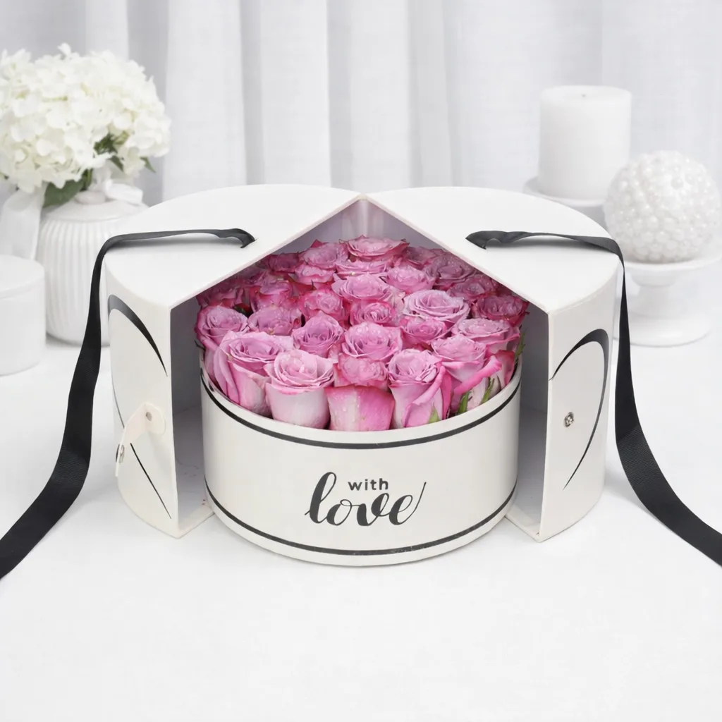 Lavender roses with water droplets in an open round white 'with love' gift box with heart-shaped split lid and black ribbon handles