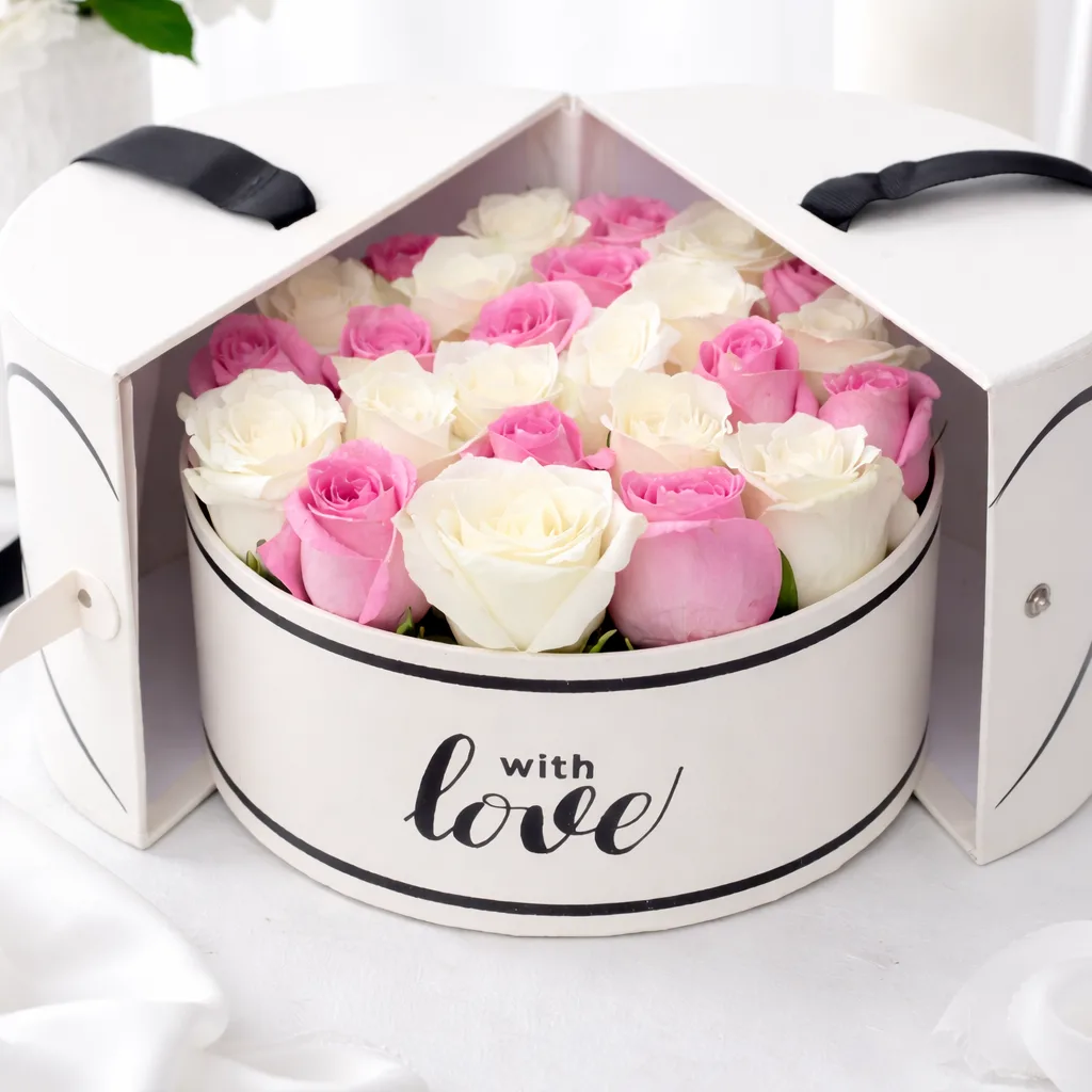 Close-up of white and pink roses filling an open round 'with love' gift box with heart-shaped split lid and black ribbon handles