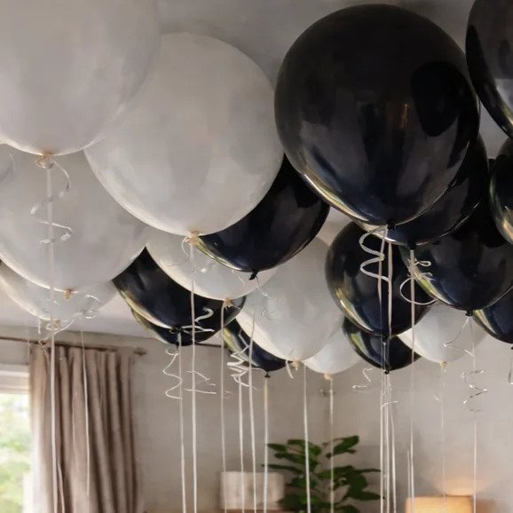 Close-up of black and white helium balloons with curly ribbons floating at the ceiling.