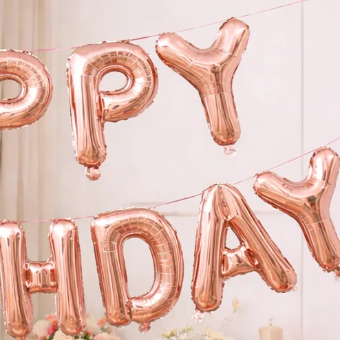 Close-up of rose gold 'Happy Birthday' foil letter balloons banner with flowers in the background