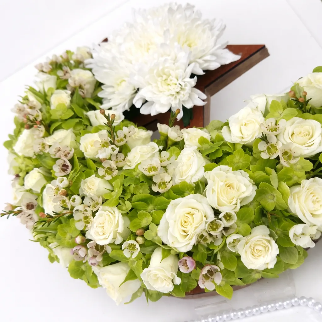 "Close-up of white roses, wax flowers, and green foliage on a crescent moon arrangement with a white chrysanthemum on the star"