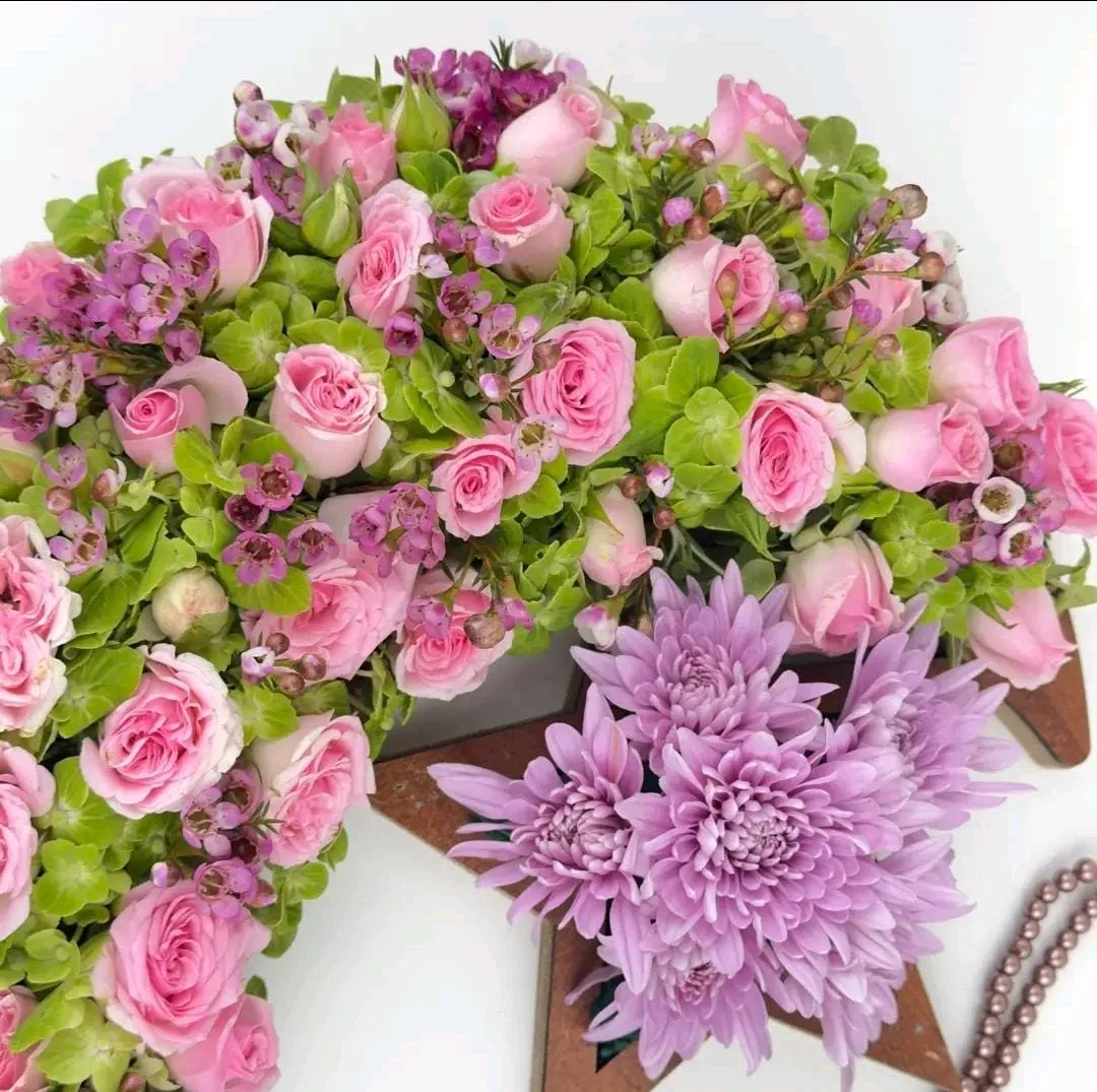 "Close-up of pink roses, wax flowers, and lavender chrysanthemums on a crescent moon floral arrangement"
