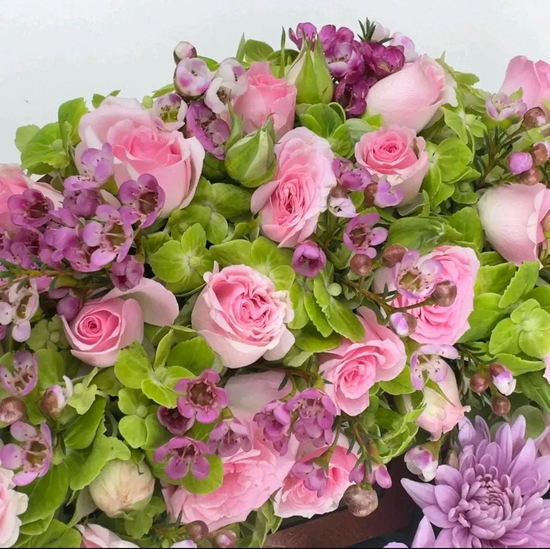 "Close-up of pink spray roses, purple wax flowers, and green foliage with a lavender chrysanthemum"