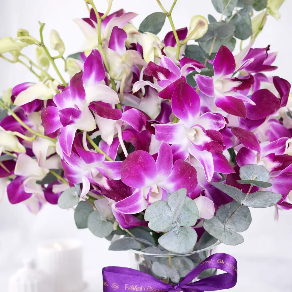 Close-up of purple dendrobium orchids with eucalyptus in a glass vase with a FaVish Blooms ribbon