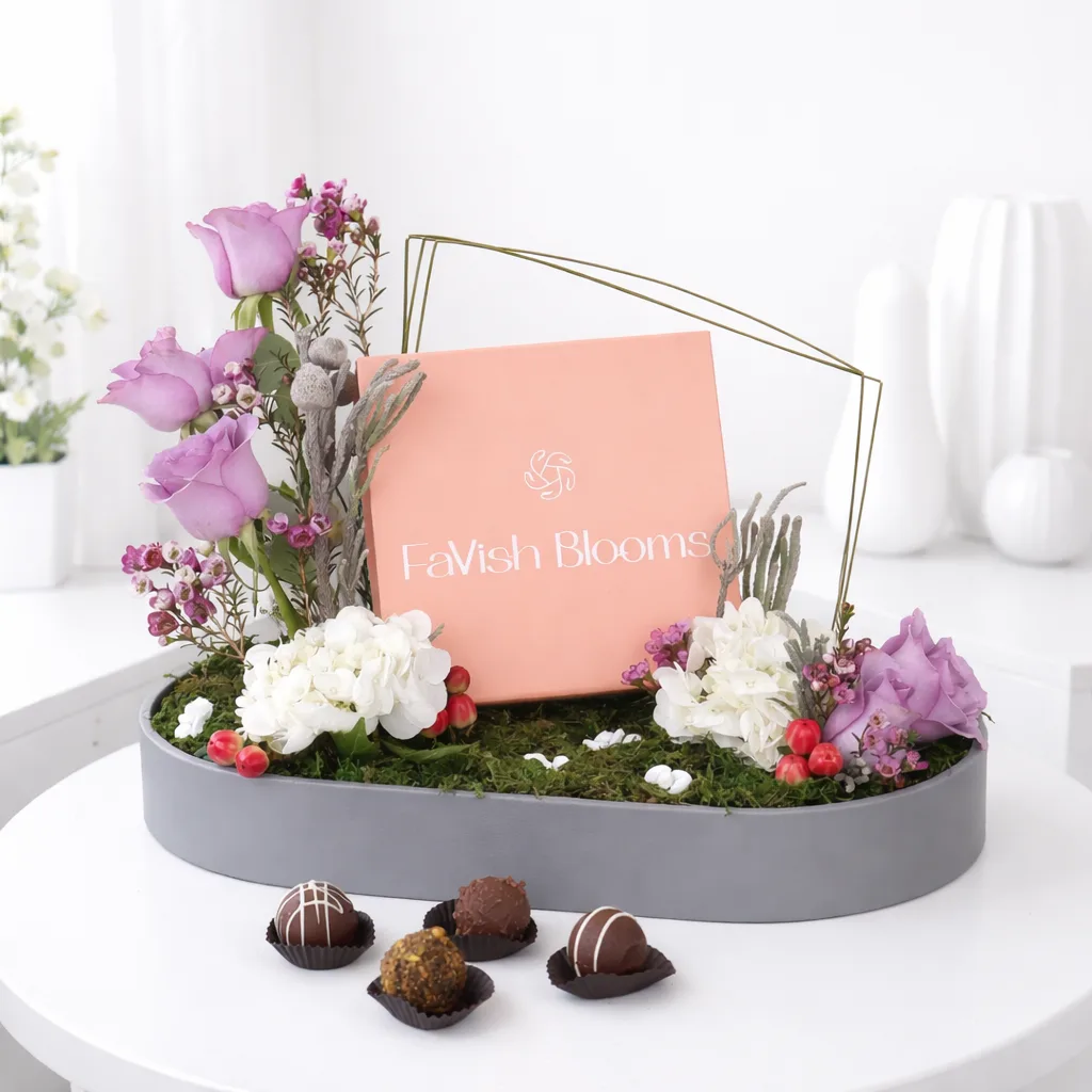 FaVish Blooms floral arrangement tray with purple roses, white hydrangeas, dried flowers, and assorted chocolate truffles.