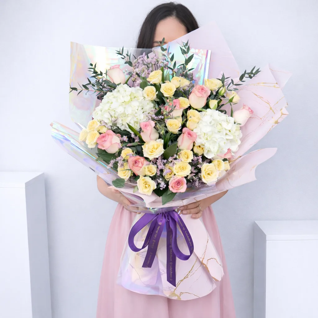 Woman holding a large luxury bouquet of cream roses, pink roses, and white hydrangea in iridescent wrapping.