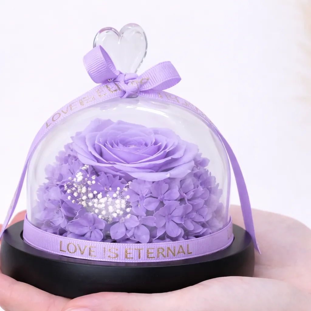 Close-up of preserved purple rose under a 'Love Is Eternal' glass dome.