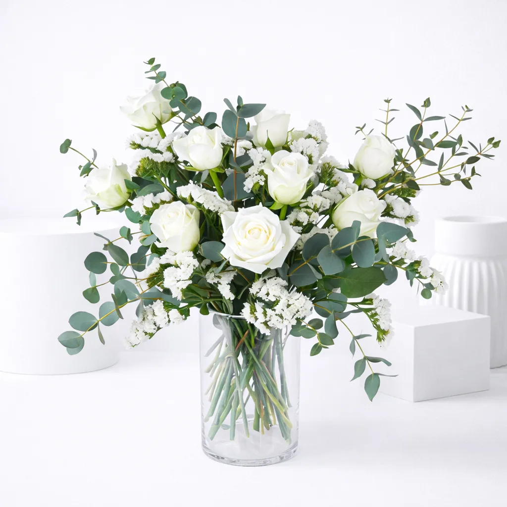 White roses and eucalyptus bouquet in a clear glass vase.
