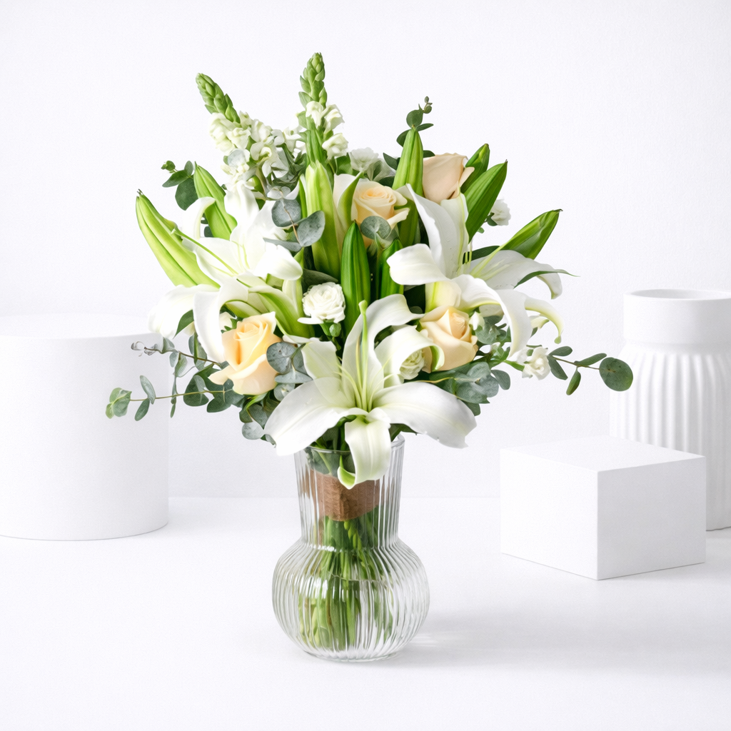 White lilies and peach roses bouquet in a ribbed glass vase.