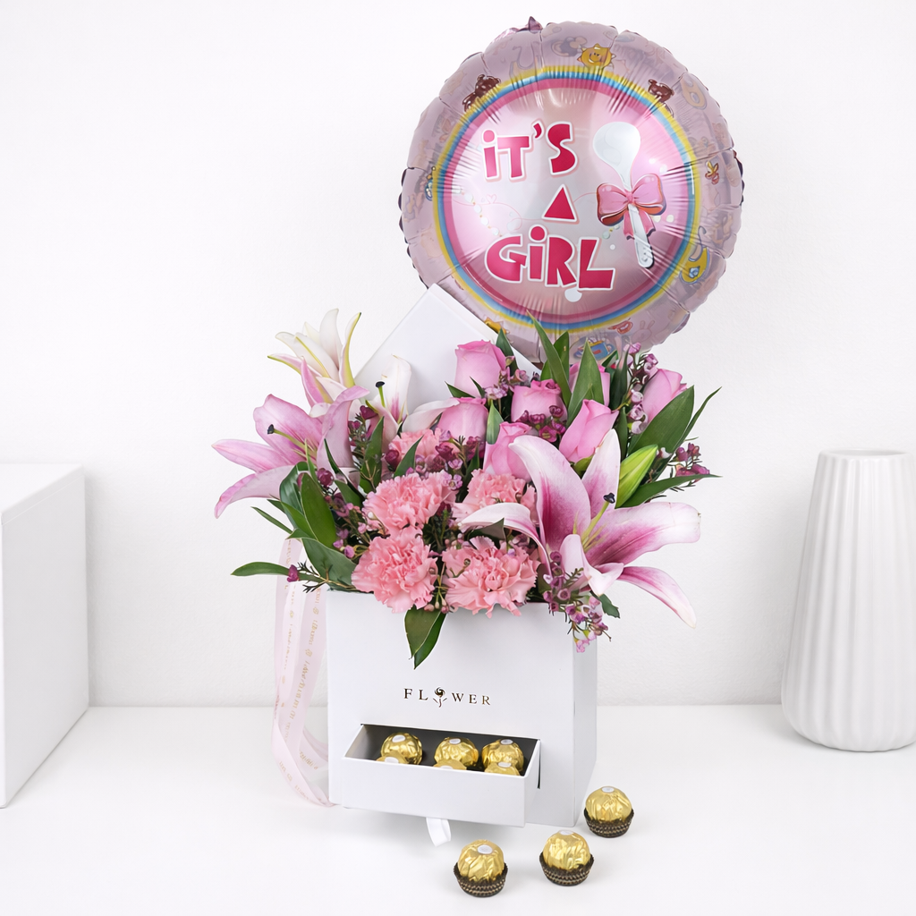 Pink lilies, roses, and carnations in a white flower box with a drawer holding Ferrero Rocher chocolates and an 'It's a Girl' balloon.