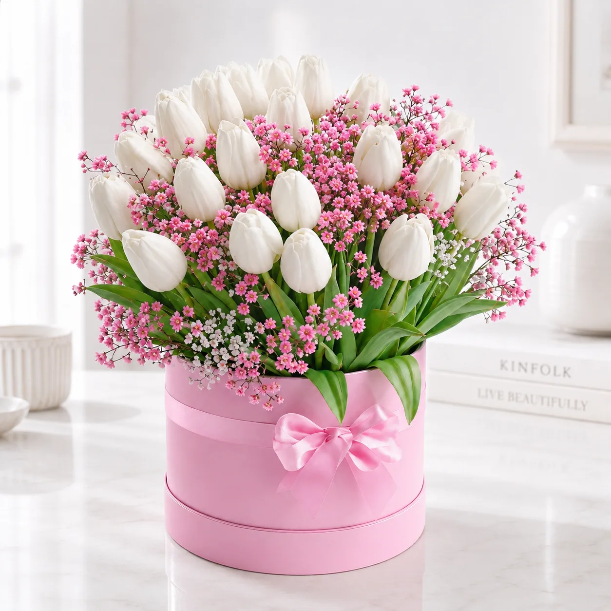 White tulips and pink baby's breath arranged in a pink hat box with a satin bow.