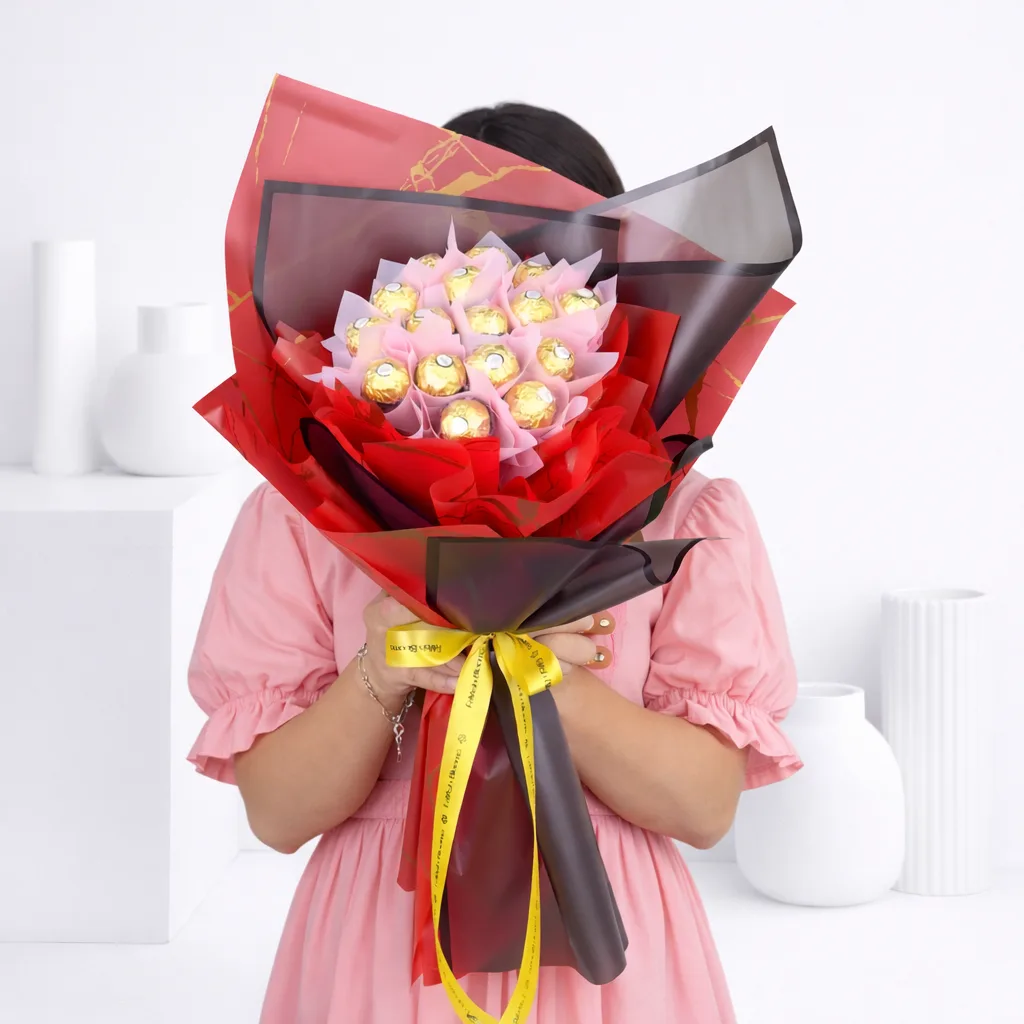 Person holding a large Ferrero Rocher chocolate bouquet in red and black wrapping with a gold ribbon.