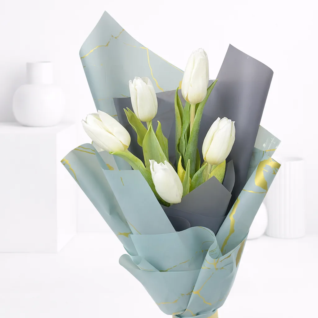 Close-up of white tulips wrapped in sage green and gold marble paper.