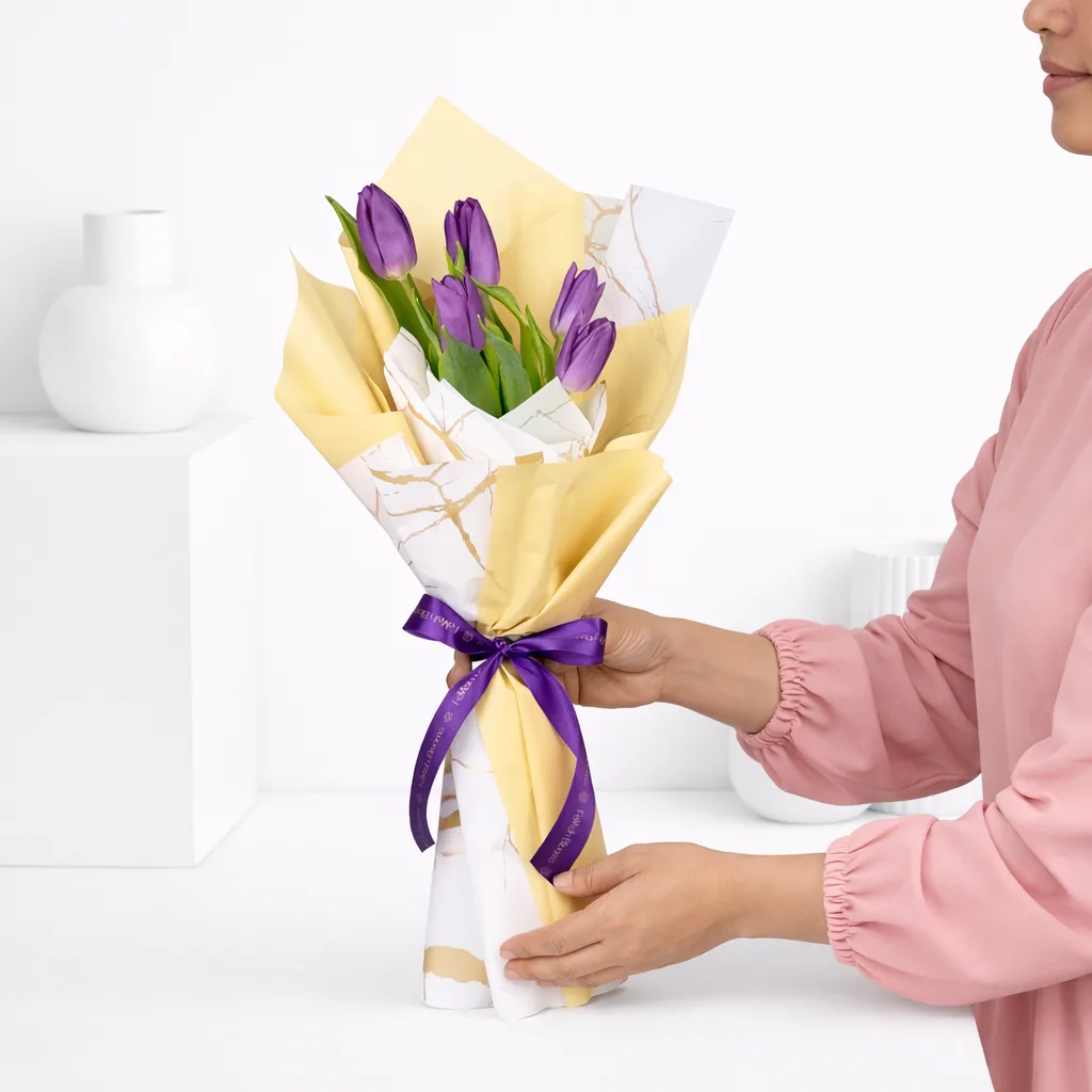 Woman in a pink top holding a purple tulip bouquet wrapped in gold and marble-print paper with a purple Favish Blooms ribbon.