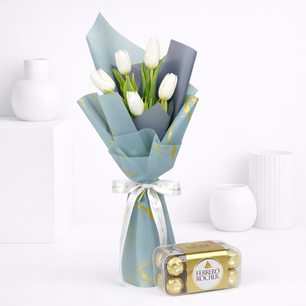 White tulips wrapped in blue-grey and gold-print paper tied with a white Favish Blooms ribbon, paired with a box of Ferrero Rocher chocolates.