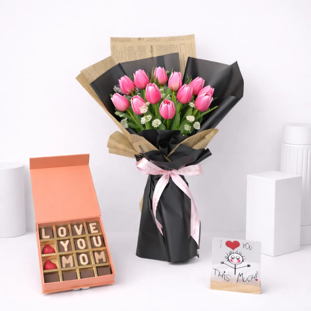 Mother's Day gift set featuring a pink tulip bouquet wrapped in black and kraft paper, a 'Love You Mom' chocolate letter box, and an 'I Love You This Much' greeting card.
