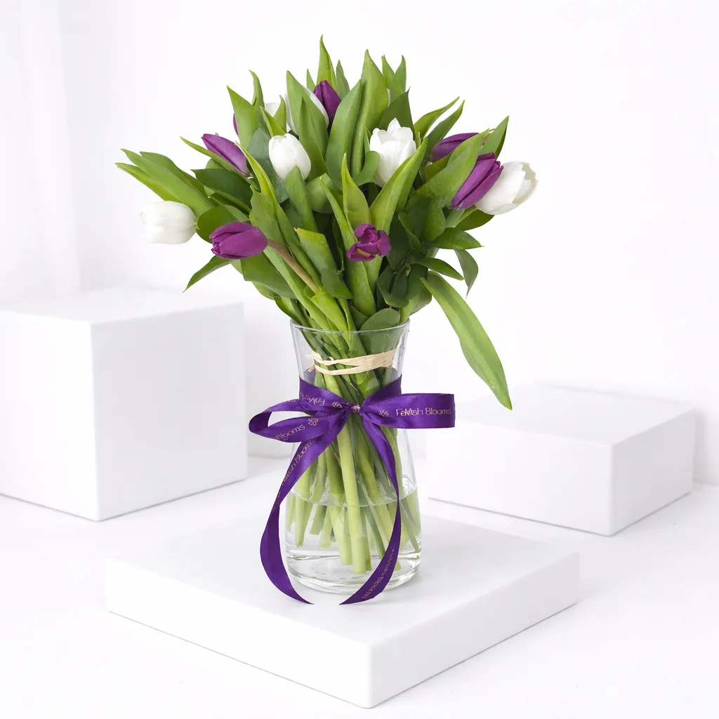 Purple and white tulips in a glass vase tied with a FaVish Blooms purple ribbon.