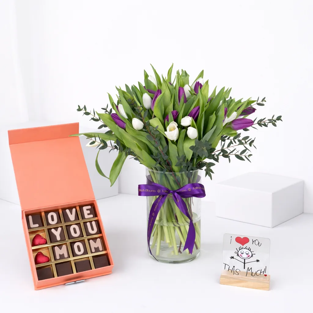 Purple and white tulip arrangement in glass vase with "Love You Mom" chocolate gift box and "I Love You This Much" greeting card.