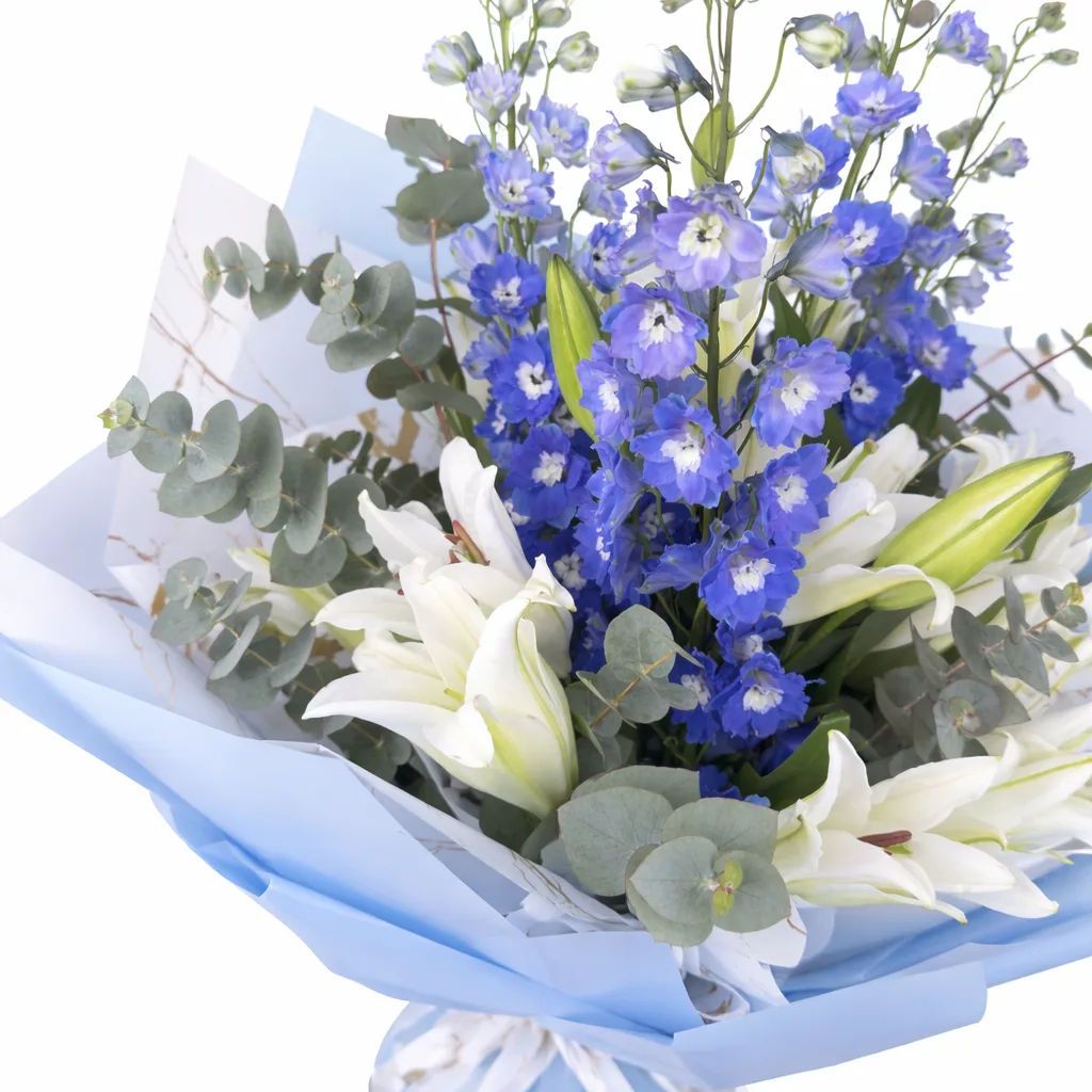 Close-up of white lilies, blue delphinium, and eucalyptus wrapped in light blue paper.