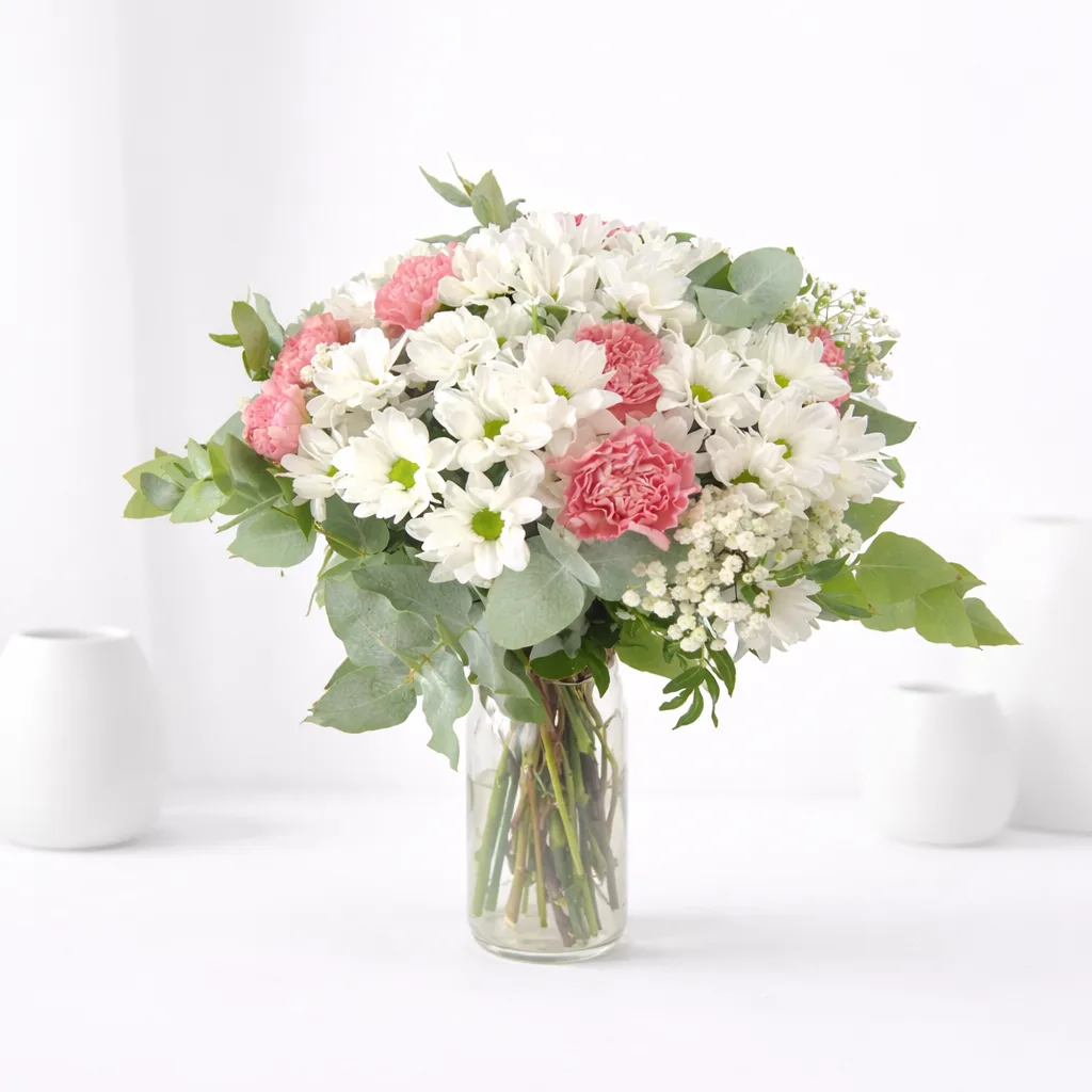 White chrysanthemum and pink carnation bouquet in a clear glass vase on a white surface