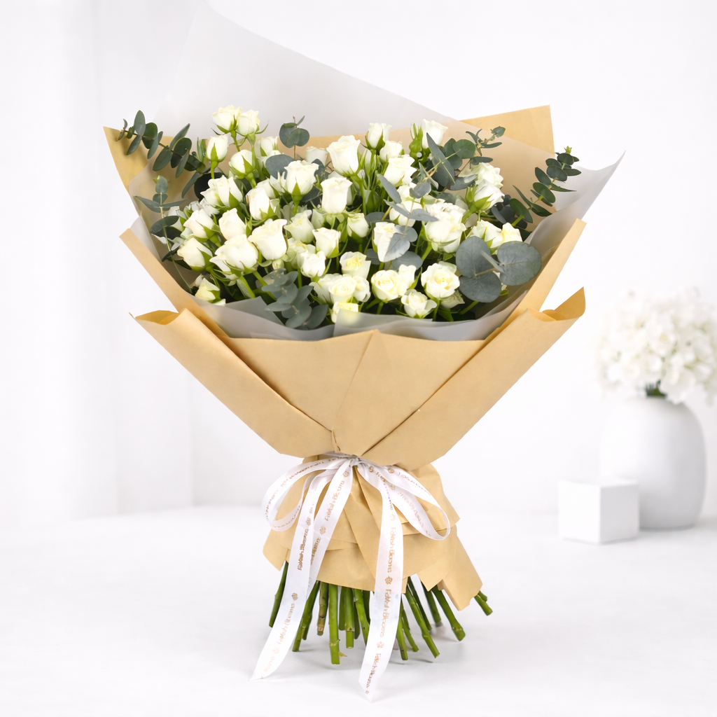 A bouquet of white spray roses and eucalyptus wrapped in kraft paper, tied with a white ribbon.