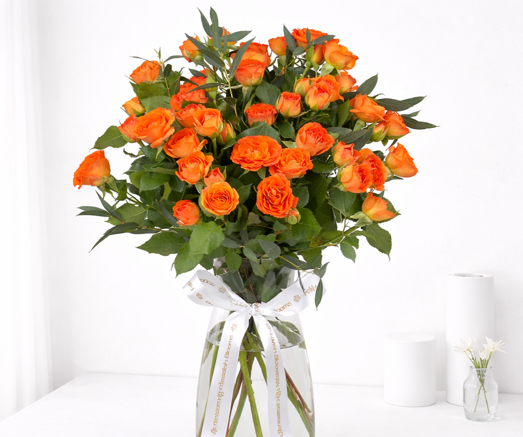 Orange roses with green foliage in a glass vase tied with a white ribbon, close-up view