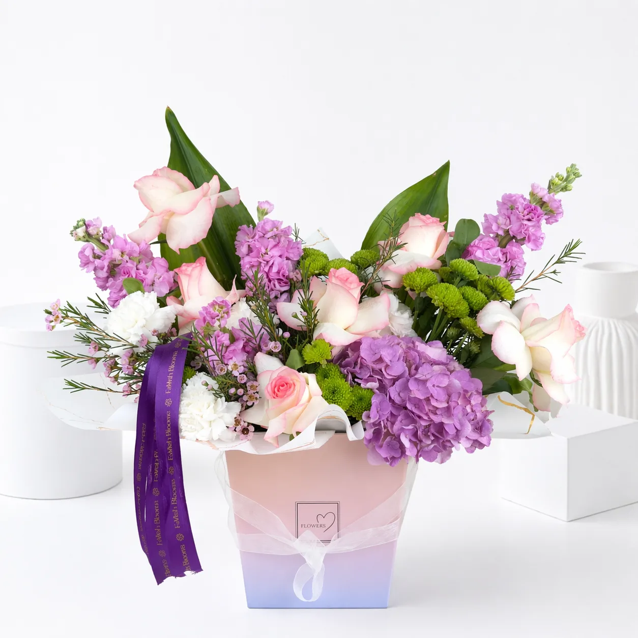 Pink and purple floral arrangement in a pastel ombre gift bag with a purple ribbon.