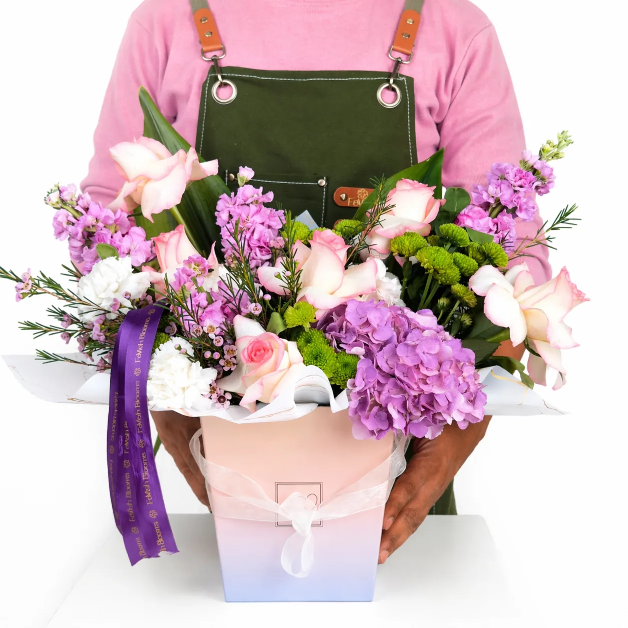 Florist holding a pink and purple floral arrangement in a pastel ombre gift bag with a purple ribbon.