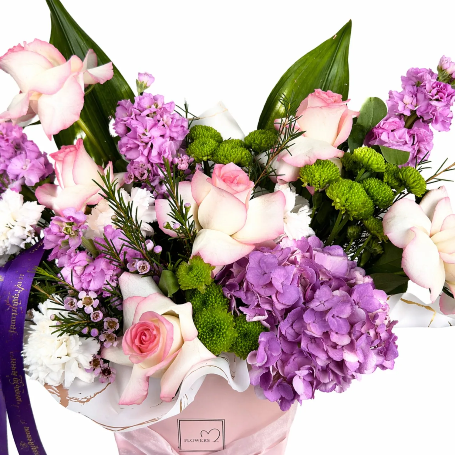 Close-up of a floral arrangement with pink roses, purple hydrangeas, stock flowers, and green button chrysanthemums in a pastel gift bag.