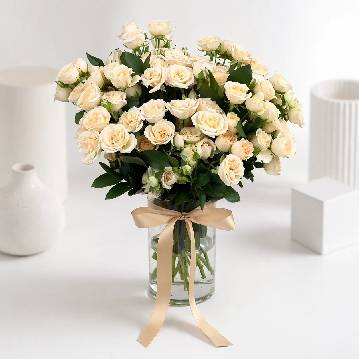 Lush bouquet of cream spray roses in a glass vase tied with a champagne satin ribbon.