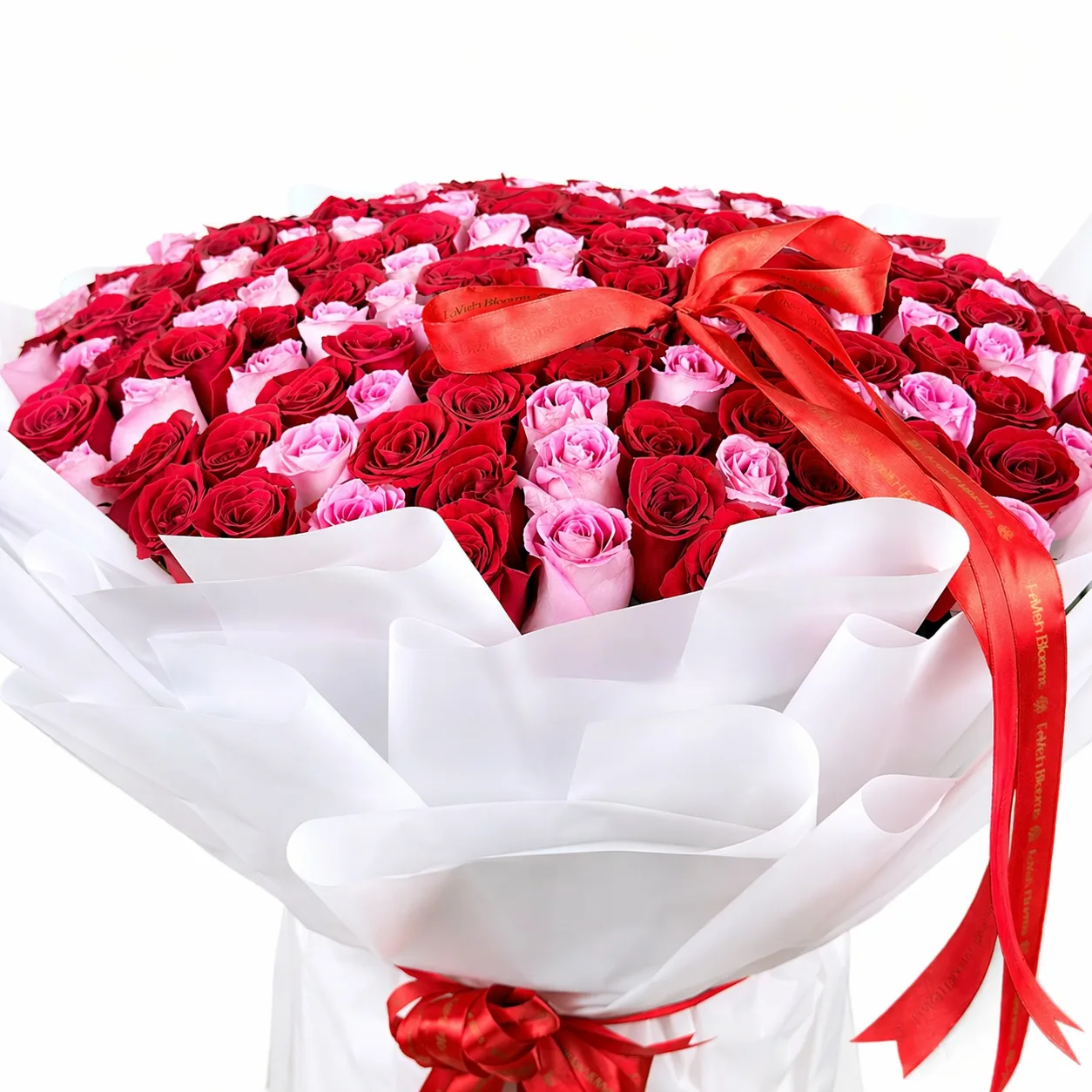 Close-up of premium red and pink rose bouquet wrapped in white paper with elegant red satin ribbon.