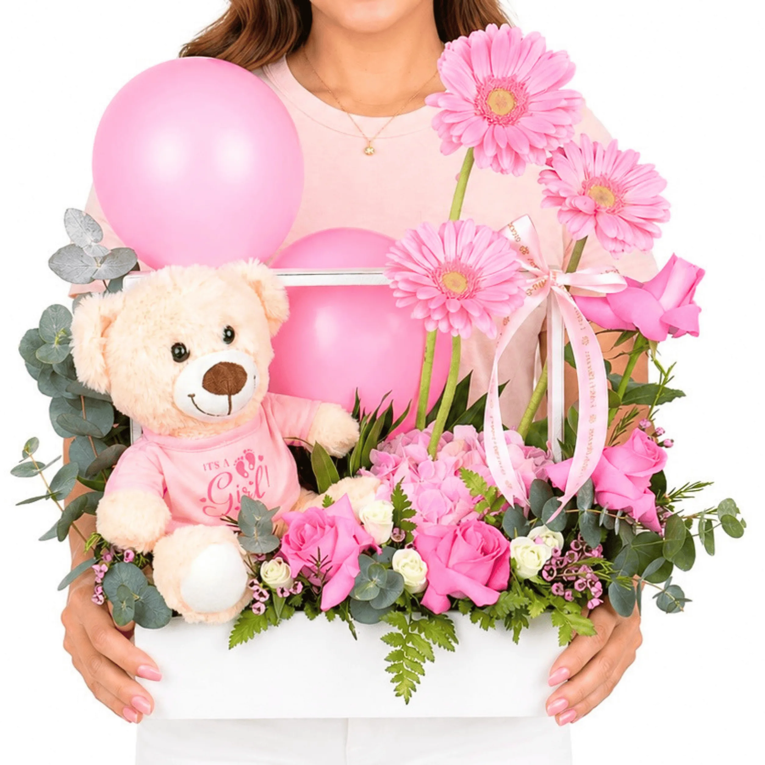 Woman holding a pink baby girl floral gift box with teddy bear, pink balloons, gerbera flowers, roses, hydrangea, and fresh greenery.