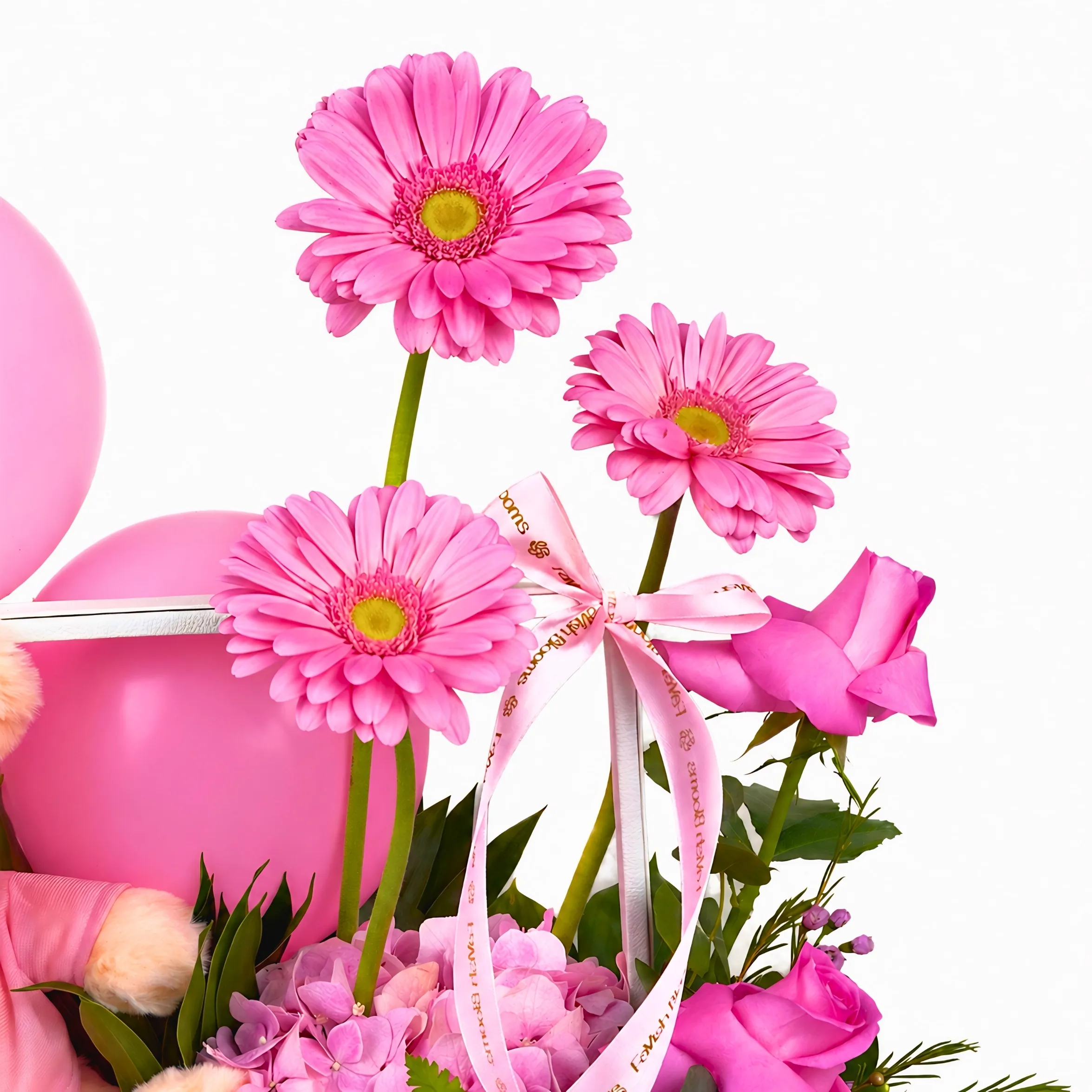 Close-up pink floral arrangement with gerbera flowers, pink balloons, roses, hydrangea, ribbon, and greenery in a baby girl gift box.