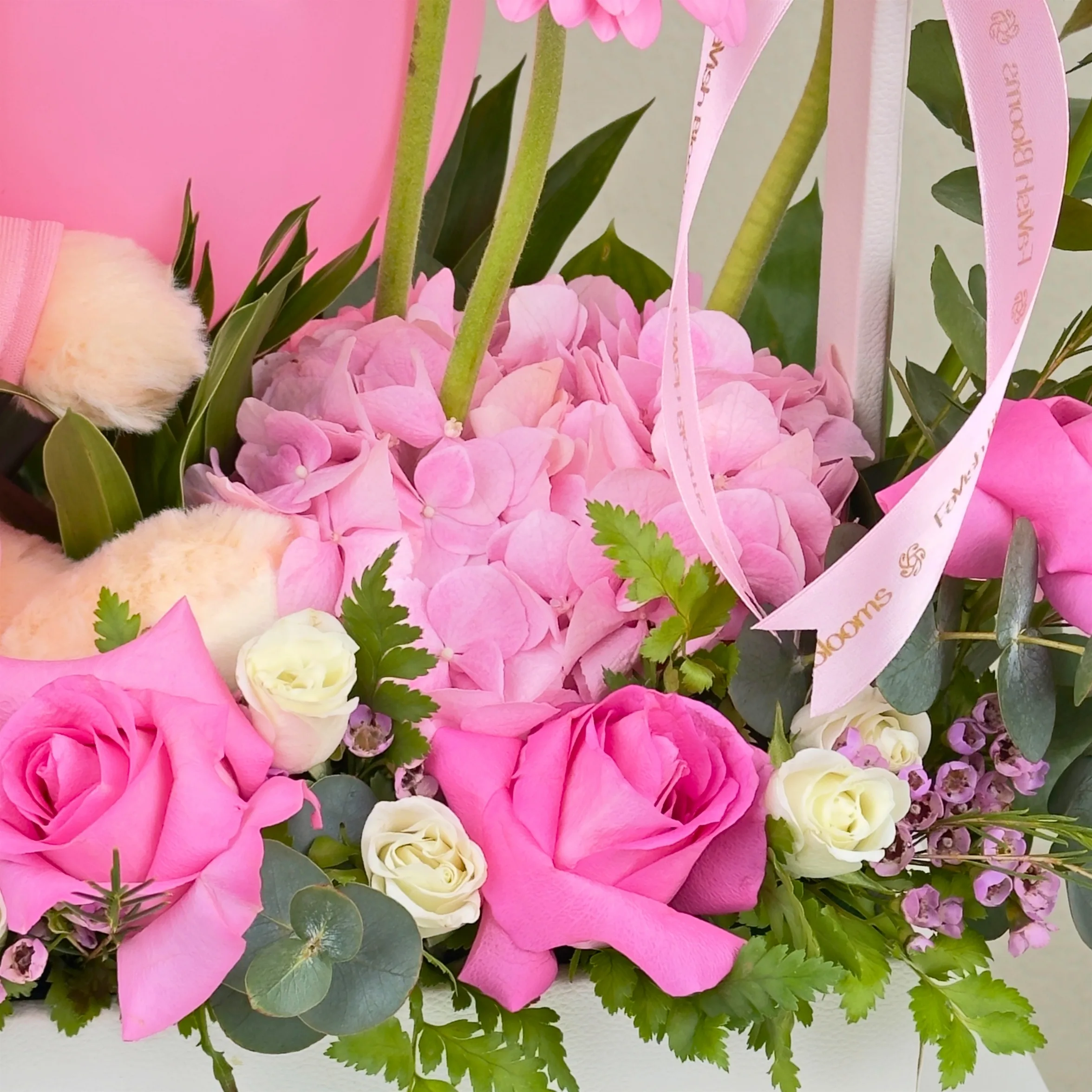 Close-up of pink roses, hydrangea, white spray roses, eucalyptus, ribbon, and fresh greenery in a luxury baby girl floral gift arrangement.