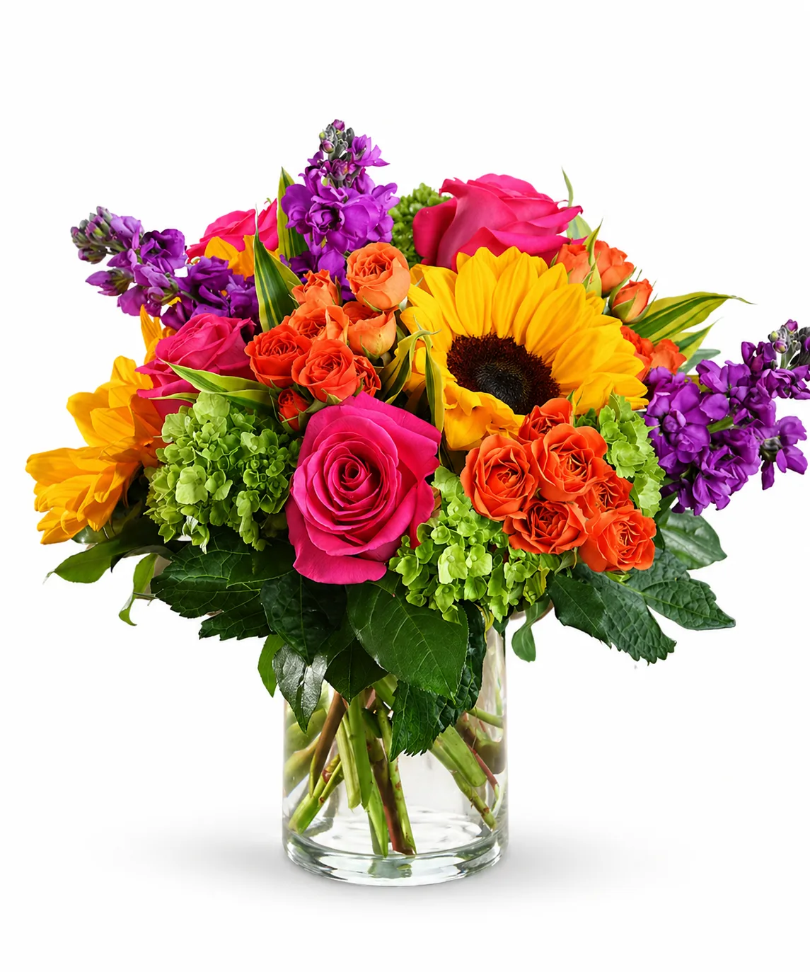 Bright mixed flower bouquet in a clear glass vase with sunflowers, pink roses, orange spray roses, purple blooms, green hydrangea, and fresh greenery on a white background.