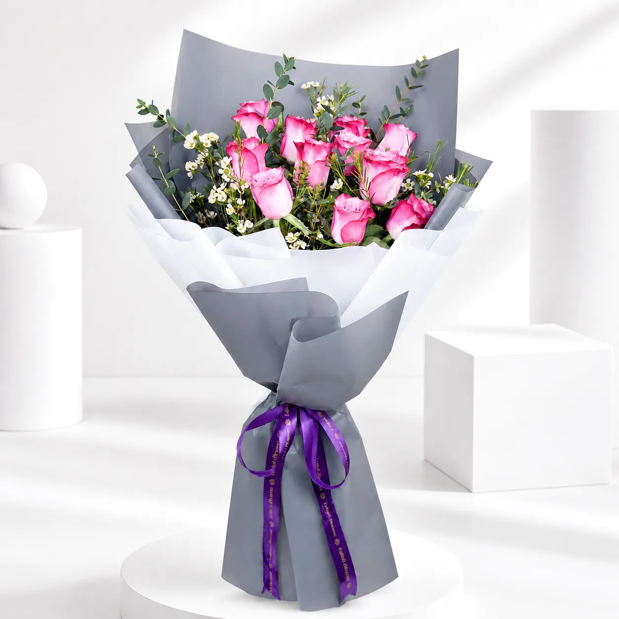 Pink roses and baby’s breath bouquet wrapped in grey paper with purple ribbon.
