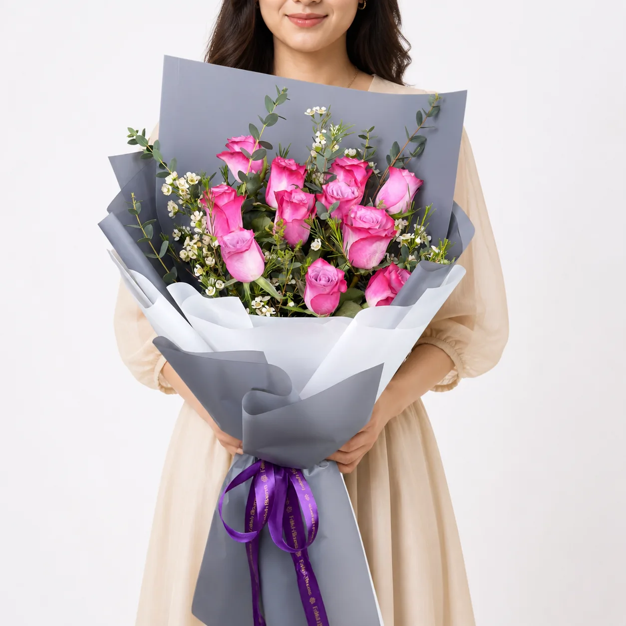 Hand holding pink roses bouquet wrapped in grey paper with purple ribbon.