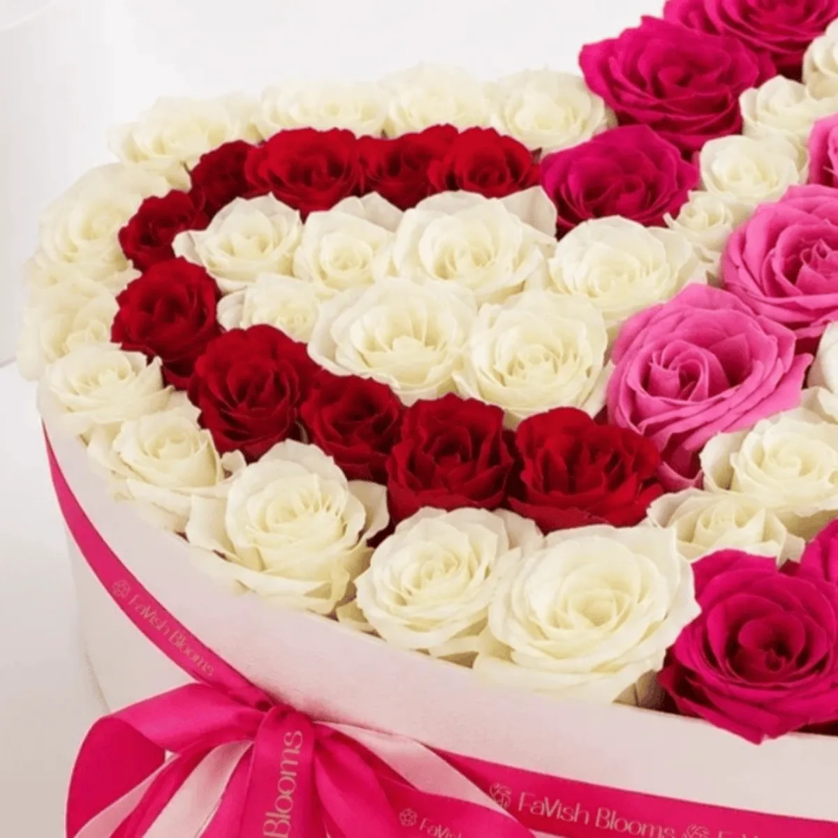 Close-up of a luxury heart-shaped rose box featuring red, white, and pink roses arranged in a romantic heart design, finished with a pink Favish Blooms ribbon.