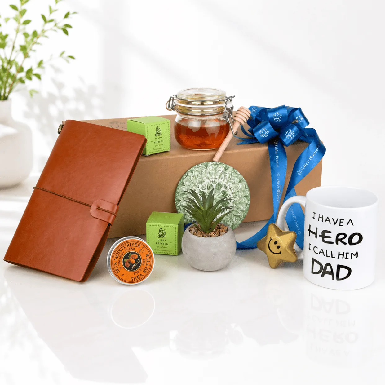 Father’s Day premium gift hamper with leather notebook, honey jar, Dad mug, mini plant, skincare items and blue ribbon gift box.