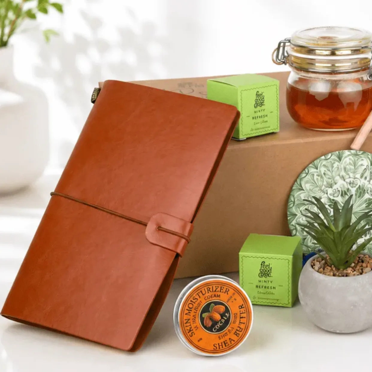 Close-up of Father’s Day gift hamper with leather notebook, honey jar, mini plant and skincare items on a premium white setup.