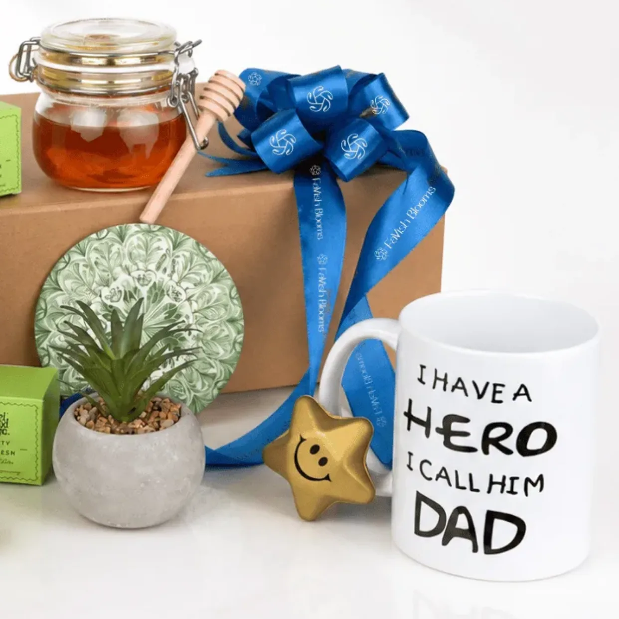 Close-up of Father’s Day gift hamper with honey jar, blue ribbon gift box, mini plant and Dad hero mug.
