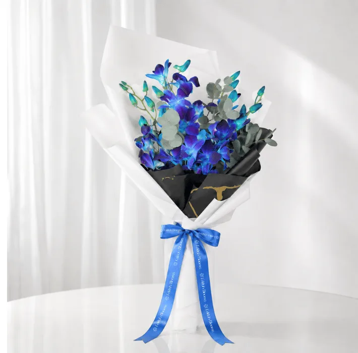 Blue orchid bouquet with eucalyptus, black and white wrapping, and blue FaVish Blooms ribbon on a white setup.
