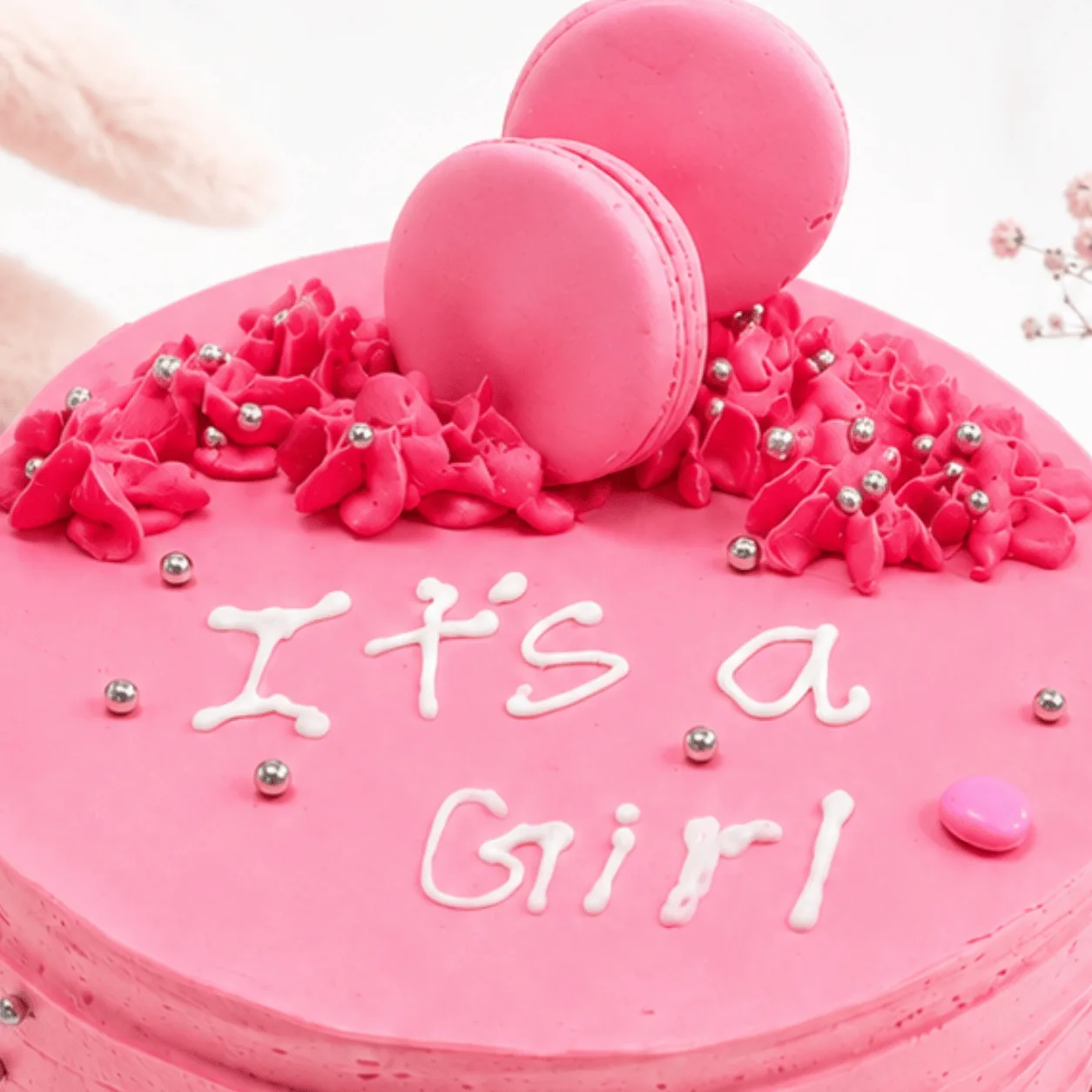 Top view of pink "It's a Girl" cake with buttercream ruffles, macarons, and silver pearls.