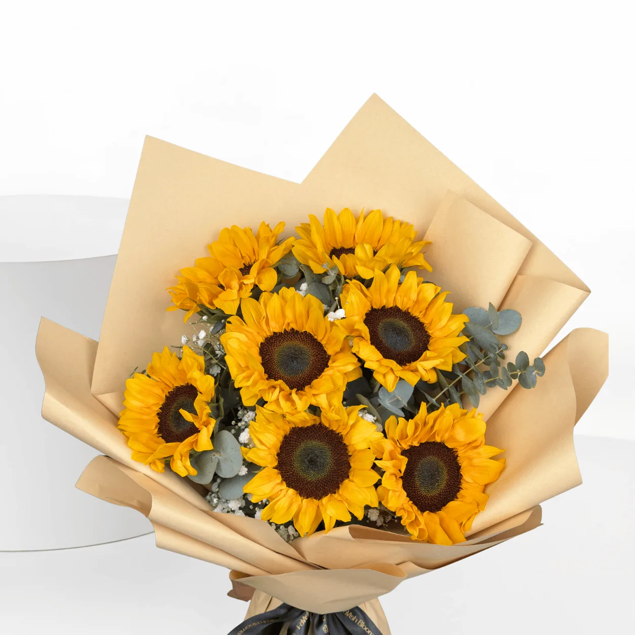 "Close-up of a sunflower bouquet wrapped in beige kraft paper with eucalyptus leaves and baby's breath, tied with a black and gold ribbon."