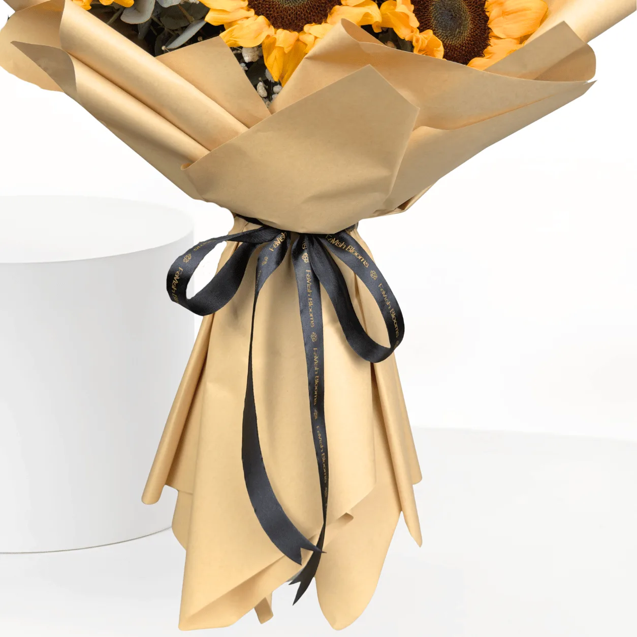 "Close-up of the beige kraft paper stem wrap on a sunflower bouquet, tied with a black ribbon printed with the 'Lavish Blooms' branding."