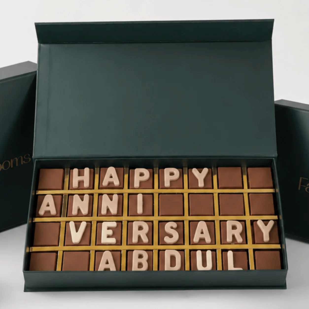 "Close-up of chocolate letter box spelling 'Happy Anniversary Abdul' in a green gift box."