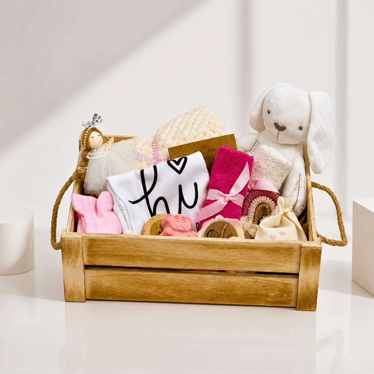Wooden crate baby girl gift basket with plush bunny, onesie, pink towel, doll, and teether toys