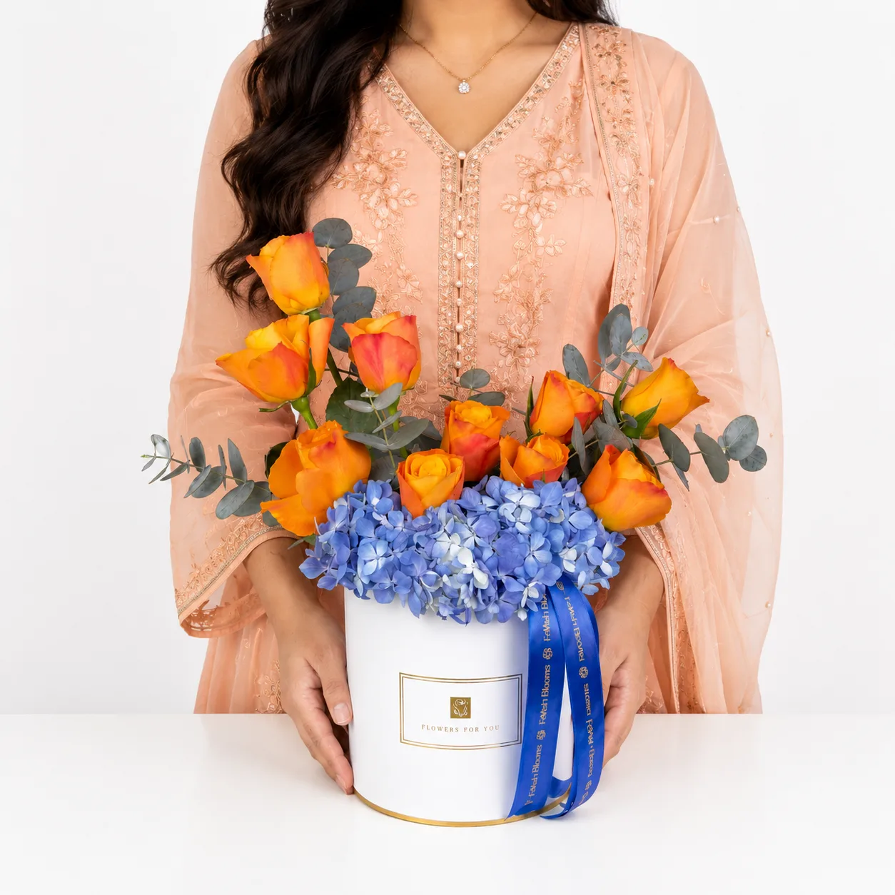Woman holding orange rose and blue hydrangea box bouquet.