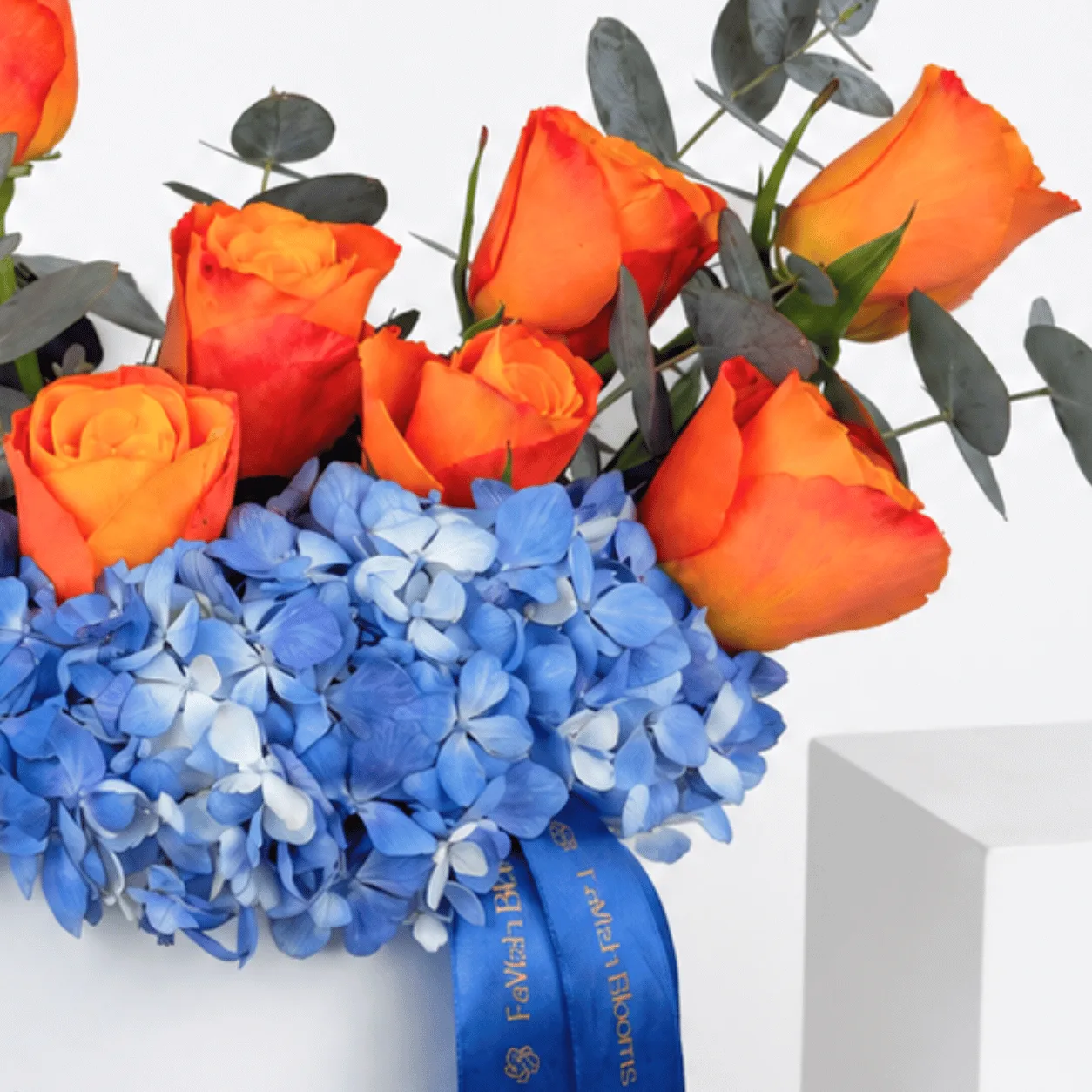 Close-up of orange roses and blue hydrangea with FaVish ribbon.